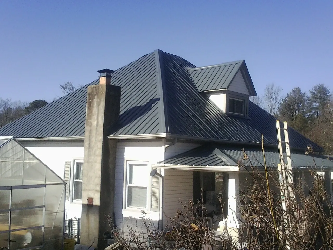 Dark blue standing seam metal roof on a white farmhouse with dormer — Slate & Tile Roof Repair by Roofing Brothers in Midway Park