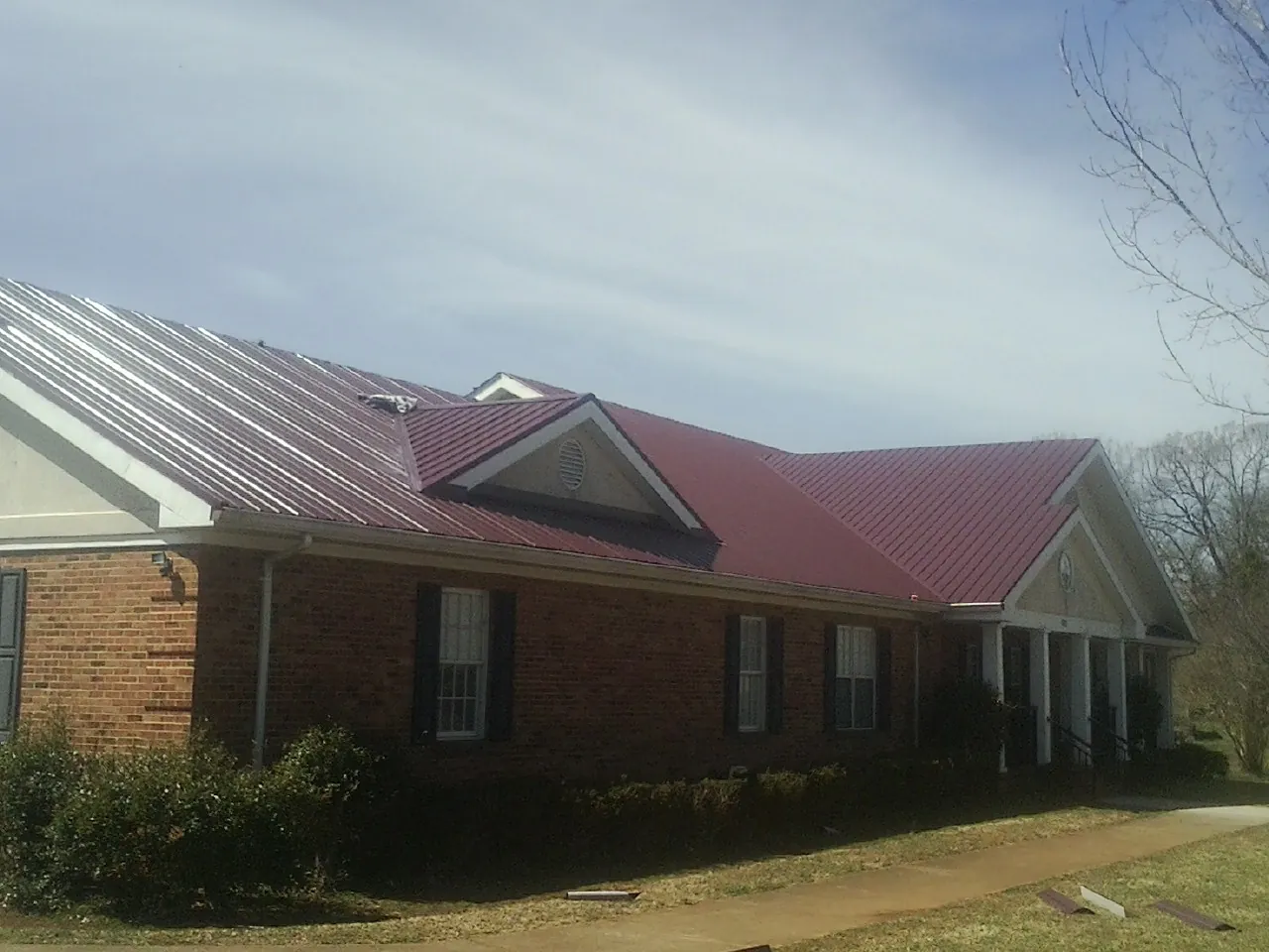 Red metal roof with gabled entries on a long brick building, from a Hail Damage Roof Repair job in Midway Park