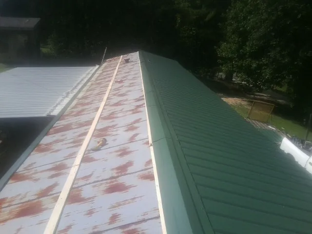 Old rusted panels beside newly installed green metal roofing — Wind Damage Roof Repair by Roofing Brothers in Midway Park