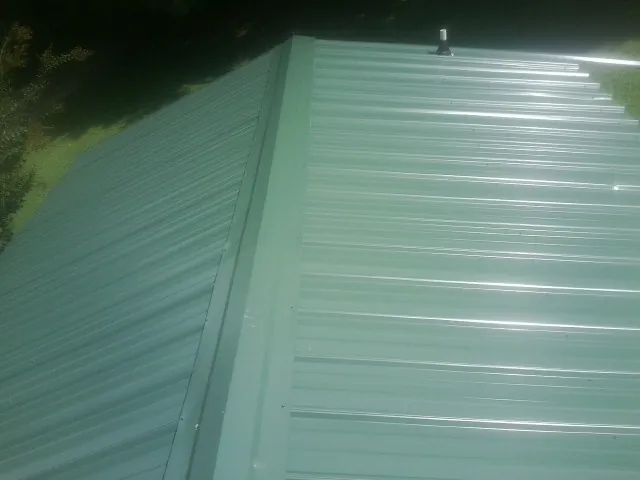 New green metal panels meeting at the ridge of a roof — Flat Roof Repair work by our crew in Midway Park