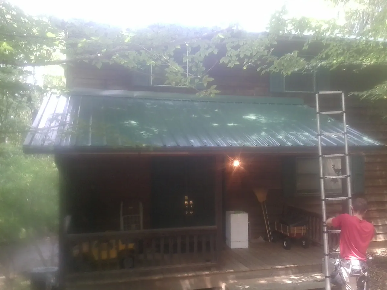 Worker on a ladder at the green porch roof of a wooded cabin in Midway Park