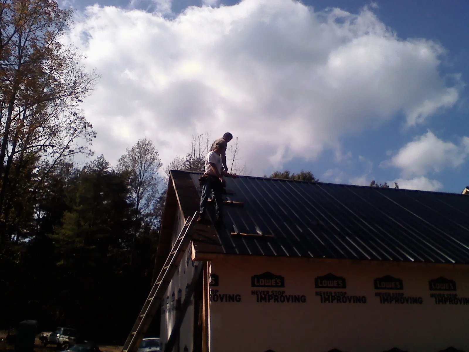 Roofer fastening dark metal panels high against a cloudy sky, from a Roof Inspection job in Midway Park