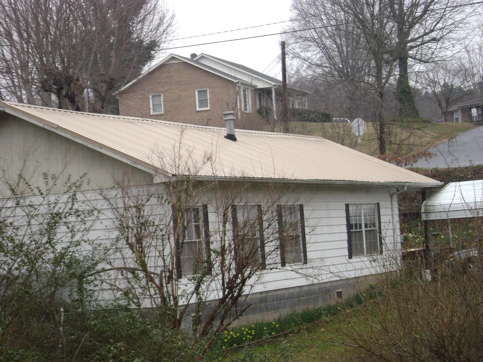Tan metal roof on a white sided house set into a hillside — Commercial Roofing by Roofing Brothers in Midway Park