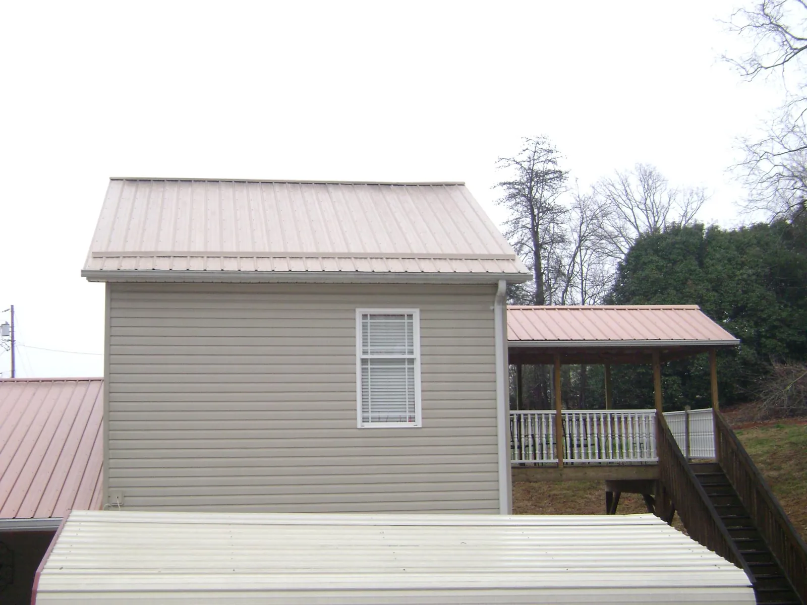Tan metal roofs on a two story addition and attached porch, from a Roof Replacement job in Midway Park
